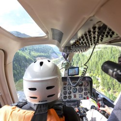 guest in front seat of helicopter as it flies towards lower canyon of Kicking Horse River