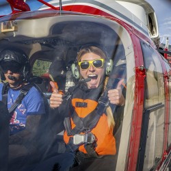 girl with big smile and thumbs up in front seat of heli, heading towards kicking horse river
