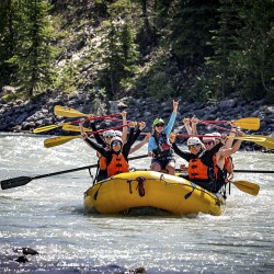 guests smiling with paddles in the air as they raft the kicking horse river