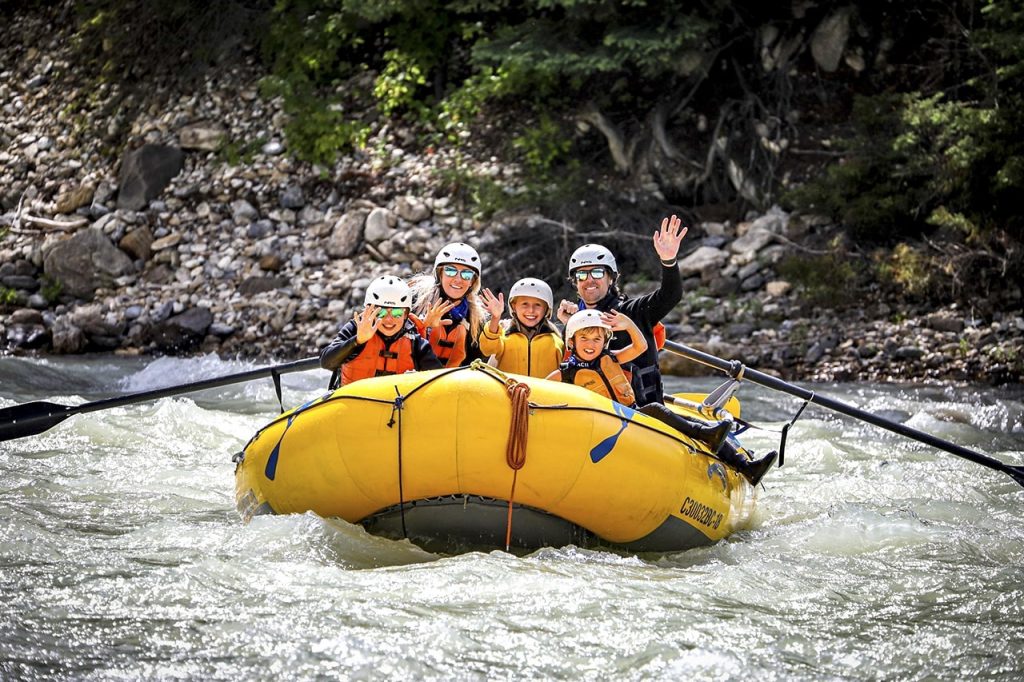 A family smiling and waving as they raft the Kicking Horse River in Golden BC