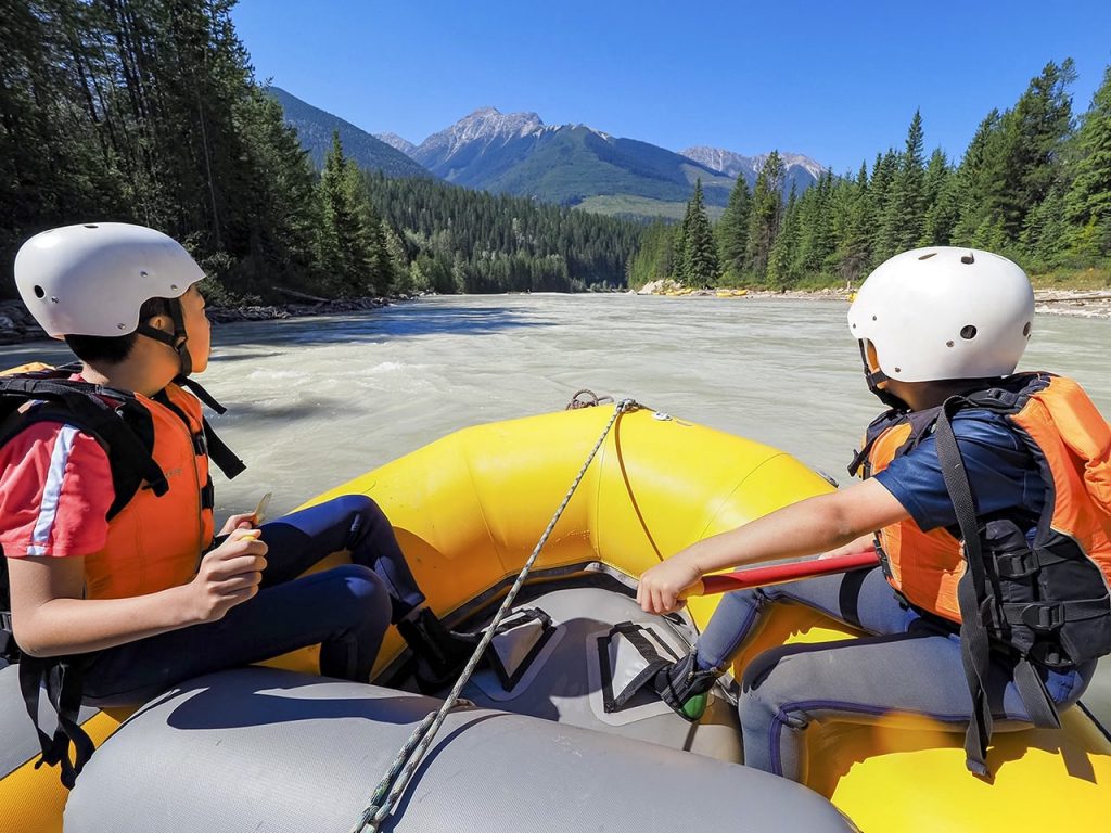 2 kids rafting the Kicking Horse River, looking at the Rocky Mountains