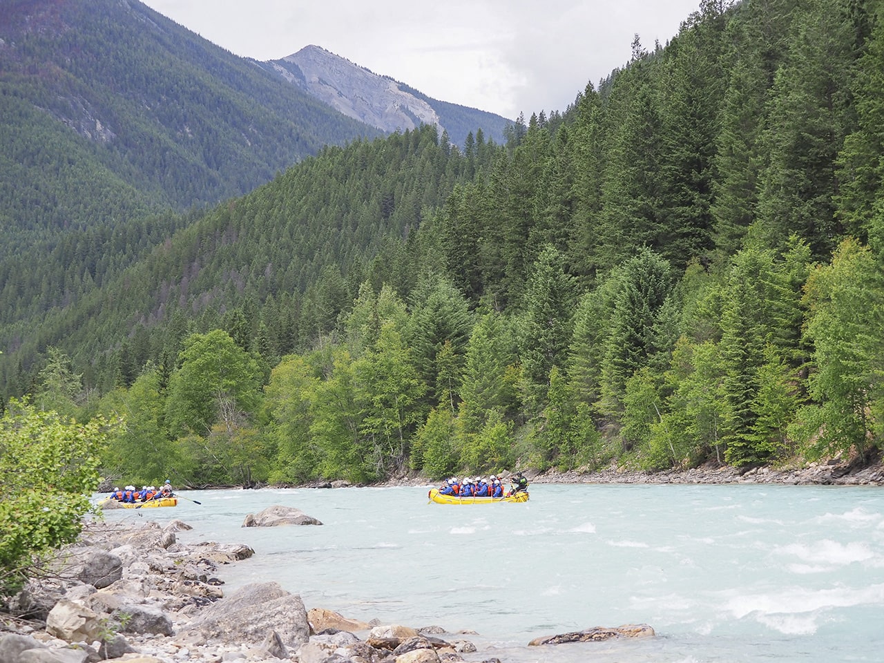 Two boats rafting down the Kicking Horse River on a grey drizzly day.